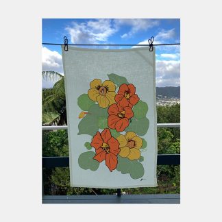 Pale green tea towel with a bold illustration of nasturtiums in orange and gold, displayed on clothesline overlooking the Hutt Valley.