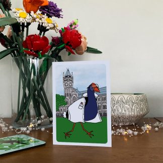 Pūkeko in a lab coat greeting card displayed on a wooden sideboard.